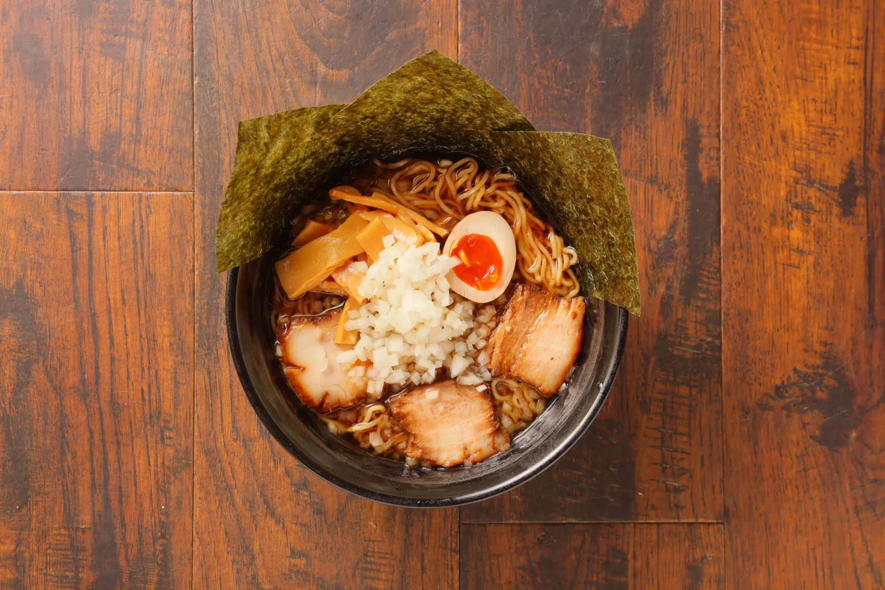全部のせDX醤油ラーメン。具材を多く盛り付けた黒い丼を真上から撮影した写真